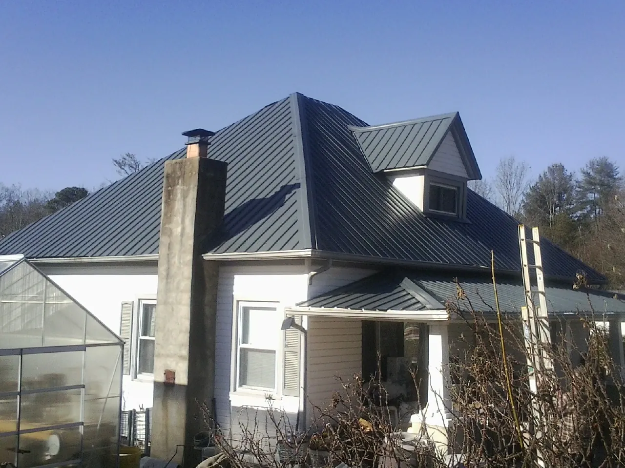 Dark blue standing seam metal roof on a white farmhouse with dormer — Slate & Tile Roof Repair by Roofing Brothers in Check