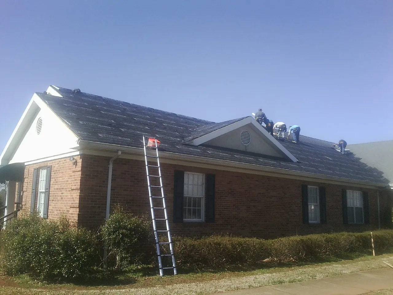 Crew tearing shingles off a brick ranch roof with a ladder set — Emergency Roof Repair work by our crew in Check