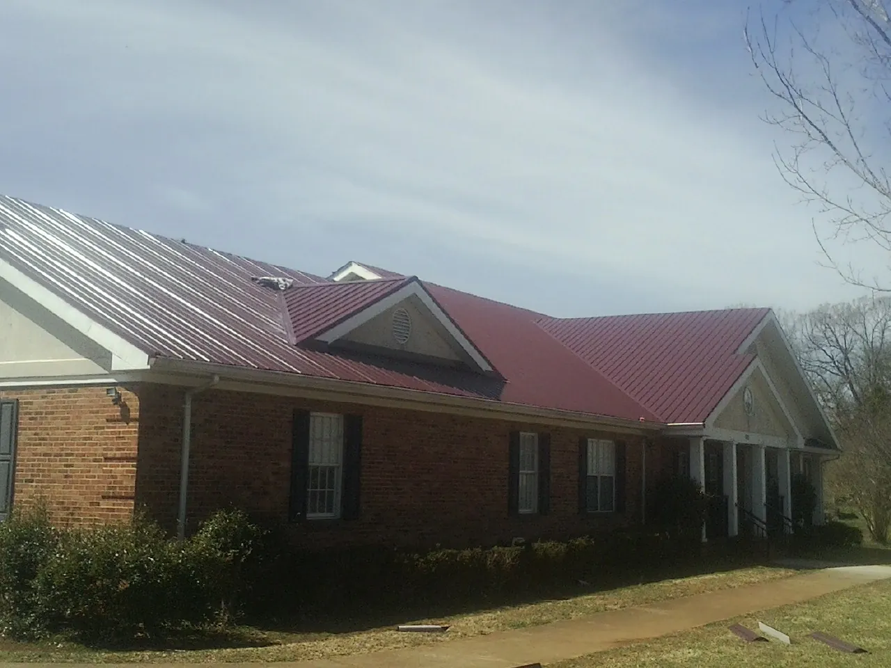 Red metal roof with gabled entries on a long brick building, from a Hail Damage Roof Repair job in Check