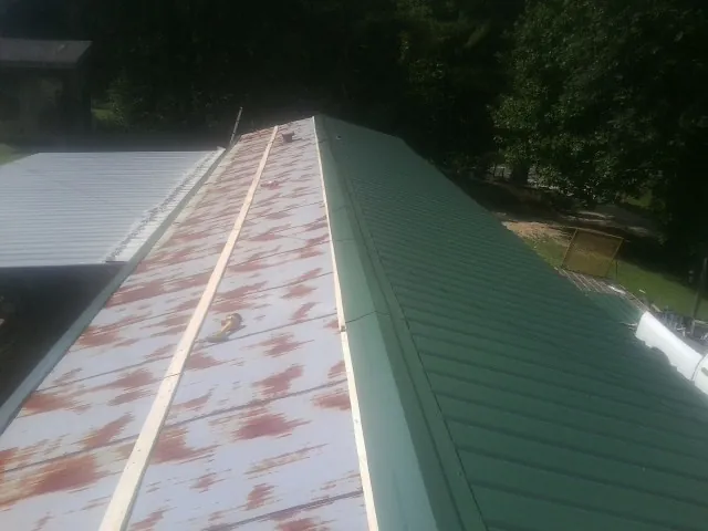 Old rusted panels beside newly installed green metal roofing — Wind Damage Roof Repair by Roofing Brothers in Check