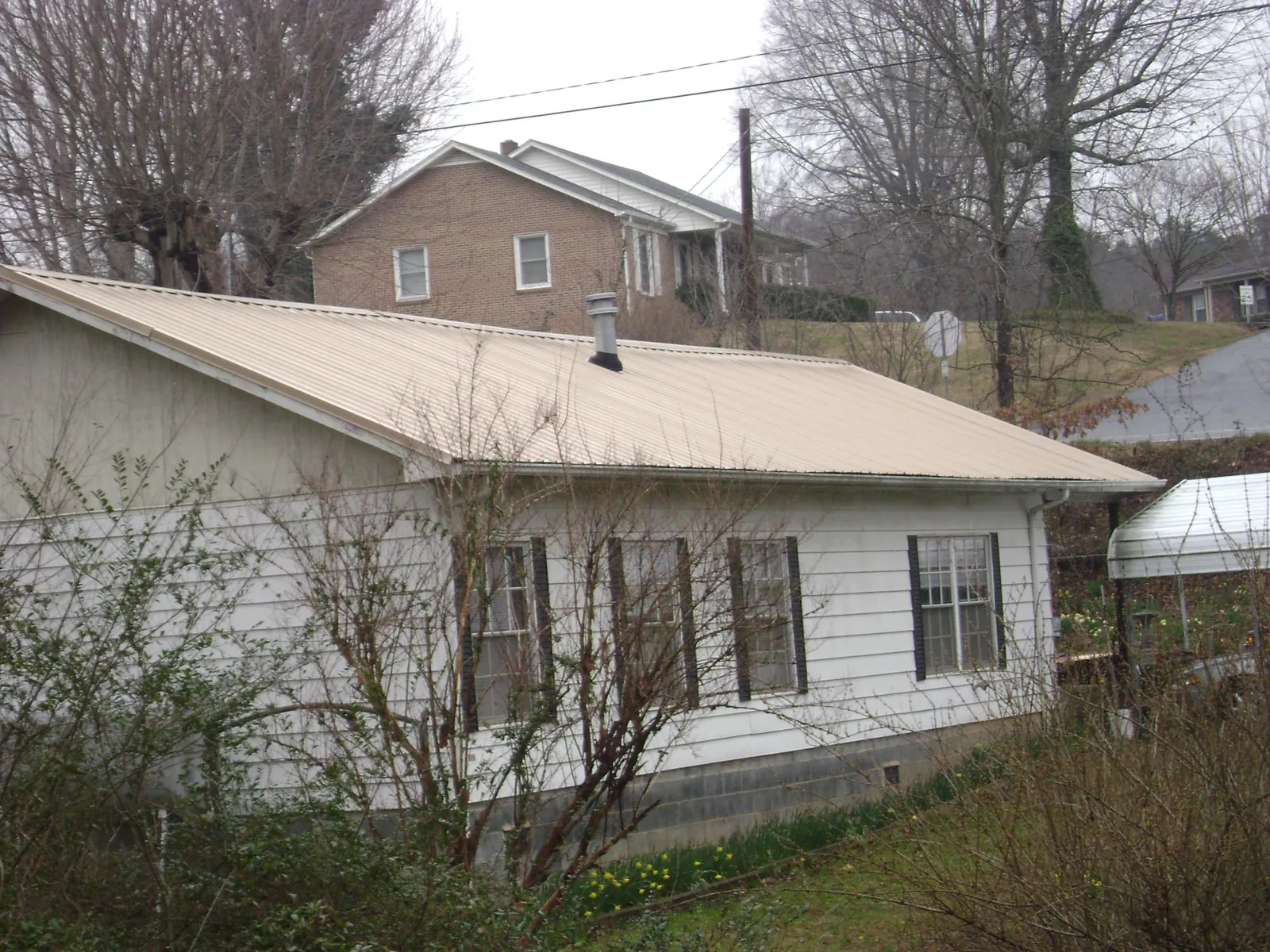 Tan metal roof on a white sided house set into a hillside — Commercial Roofing by Roofing Brothers in Check